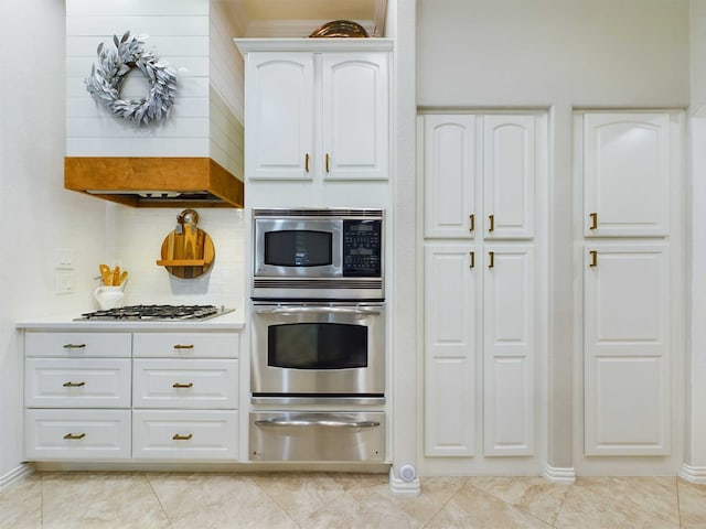 kitchen with white cabinets, appliances with stainless steel finishes, custom exhaust hood, and tasteful backsplash