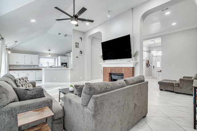 tiled living room featuring ceiling fan with notable chandelier, a brick fireplace, ornamental molding, and lofted ceiling