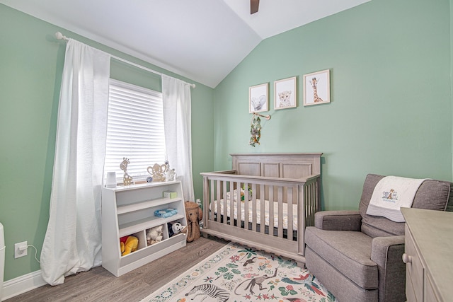 bedroom with ceiling fan, light hardwood / wood-style flooring, lofted ceiling, and a nursery area