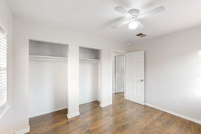 unfurnished bedroom with dark hardwood / wood-style flooring, two closets, and ceiling fan