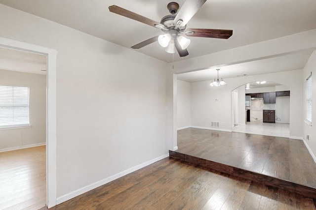 unfurnished living room featuring ceiling fan with notable chandelier and dark hardwood / wood-style flooring