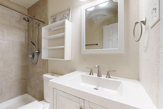 bathroom with tiled shower, vanity, and toilet