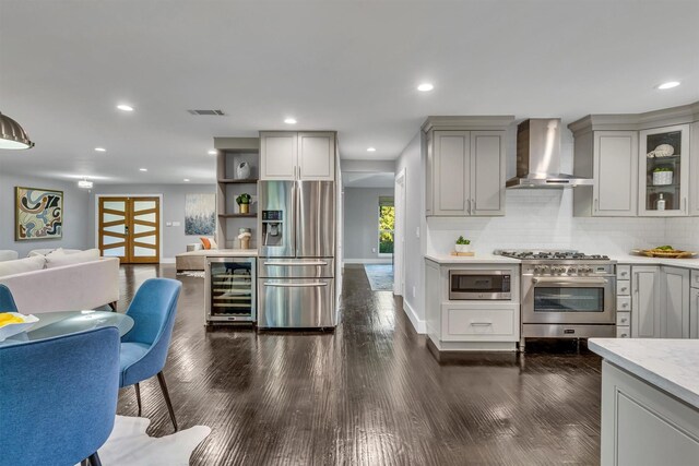 kitchen with wall chimney exhaust hood, stainless steel appliances, beverage cooler, gray cabinets, and backsplash