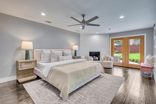 bedroom with access to outside, french doors, ceiling fan, a large fireplace, and dark wood-type flooring