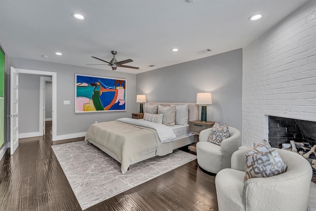 bedroom featuring dark hardwood / wood-style flooring, a brick fireplace, and ceiling fan