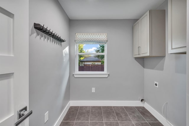 washroom with dark tile patterned floors, electric dryer hookup, and cabinets