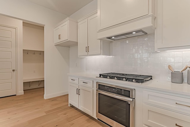 kitchen with white cabinets, light hardwood / wood-style floors, premium range hood, and appliances with stainless steel finishes