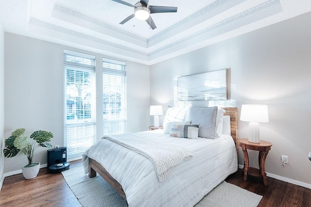 bedroom with ceiling fan, crown molding, a raised ceiling, and dark wood-type flooring