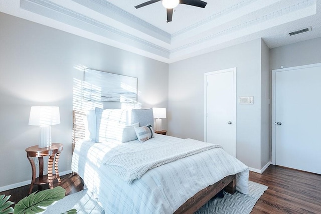 bedroom with ceiling fan, dark wood-type flooring, crown molding, and a tray ceiling