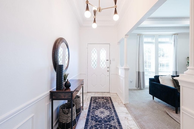 carpeted foyer featuring ornamental molding, an inviting chandelier, and decorative columns