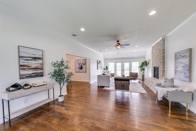 living room featuring ornamental molding, dark wood-type flooring, a stone fireplace, and ceiling fan