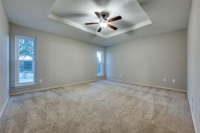 empty room with a raised ceiling, ceiling fan, a textured ceiling, and light carpet