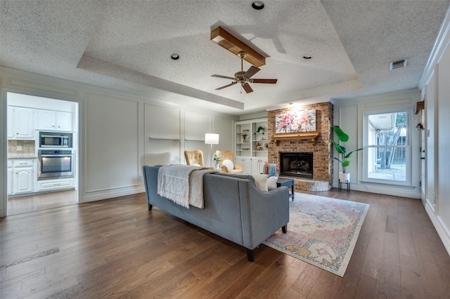 living room featuring a fireplace, ceiling fan, a tray ceiling, and dark hardwood / wood-style flooring