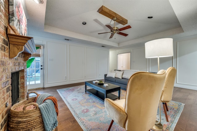 living room featuring dark wood-type flooring, a raised ceiling, and ceiling fan