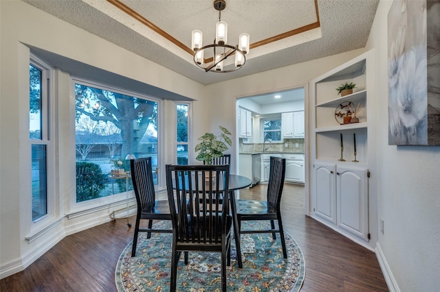 dining area with a textured ceiling, a raised ceiling, a notable chandelier, dark hardwood / wood-style flooring, and sink