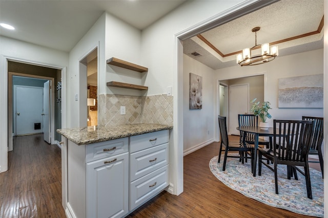 kitchen featuring white cabinetry, an inviting chandelier, light stone counters, decorative backsplash, and dark hardwood / wood-style floors