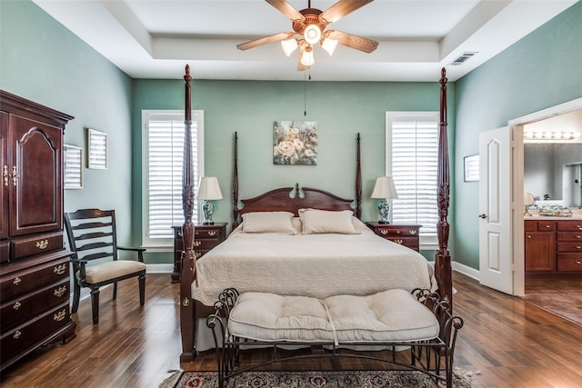 bedroom with ceiling fan, dark hardwood / wood-style flooring, a raised ceiling, and ensuite bath