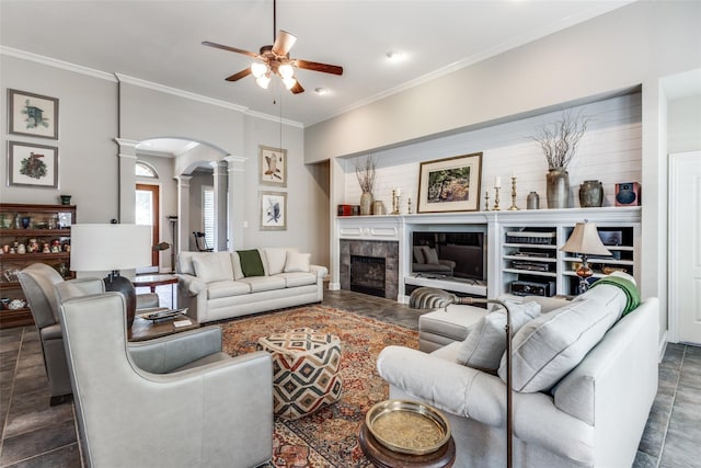 living room featuring ceiling fan, a tile fireplace, crown molding, and ornate columns