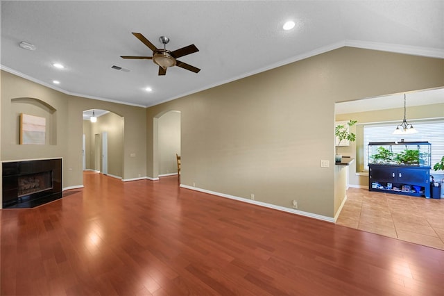 unfurnished living room with ceiling fan with notable chandelier, hardwood / wood-style flooring, a tiled fireplace, and ornamental molding