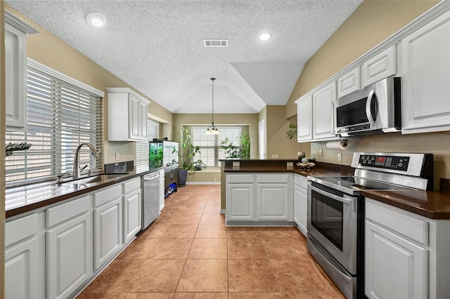 kitchen with appliances with stainless steel finishes, white cabinets, vaulted ceiling, and sink