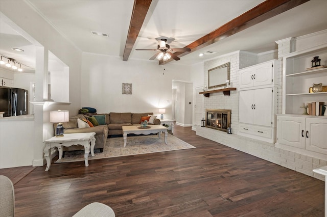 living room with ceiling fan, dark hardwood / wood-style flooring, a brick fireplace, and beamed ceiling