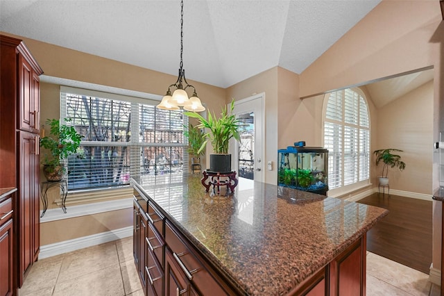 kitchen with dark stone counters, a kitchen island, vaulted ceiling, and light tile patterned floors