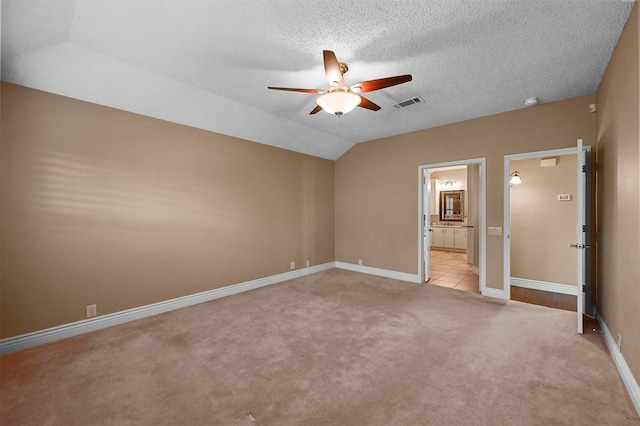 unfurnished bedroom featuring a textured ceiling, lofted ceiling, ceiling fan, ensuite bath, and light colored carpet