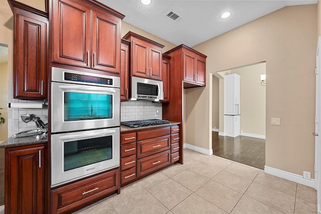 kitchen with stainless steel appliances, dark stone countertops, light tile patterned flooring, and tasteful backsplash