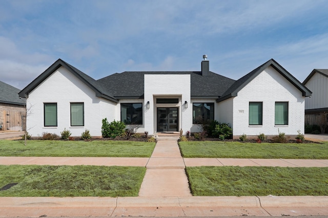 modern inspired farmhouse featuring brick siding, a front lawn, a chimney, and a shingled roof