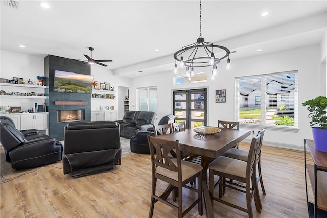 dining space with a tiled fireplace, light hardwood / wood-style floors, and ceiling fan with notable chandelier