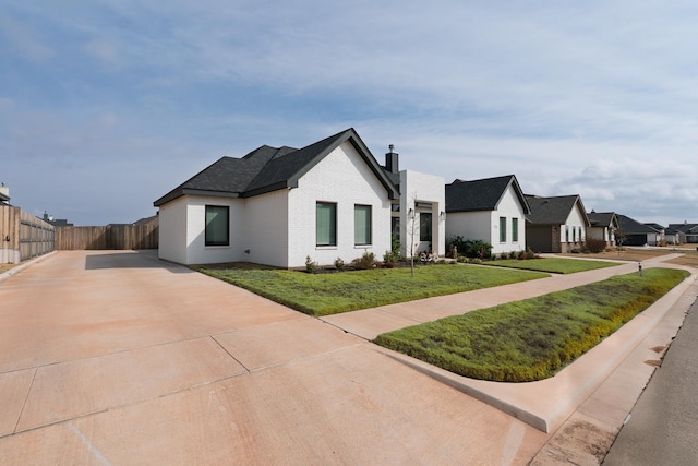 view of front of property featuring brick siding, fence, a residential view, a chimney, and a front yard