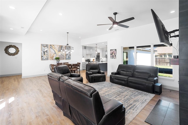 living room with sink, light wood-type flooring, and ceiling fan with notable chandelier