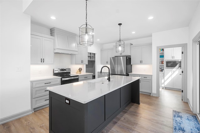 kitchen featuring sink, decorative light fixtures, custom exhaust hood, a center island with sink, and appliances with stainless steel finishes