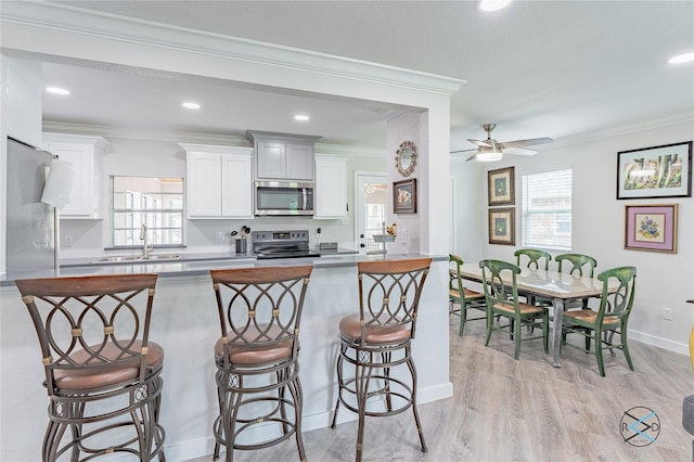 kitchen featuring white cabinets, ornamental molding, a breakfast bar, and appliances with stainless steel finishes