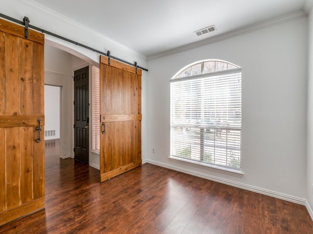 empty room with ornamental molding, a barn door, and dark hardwood / wood-style floors