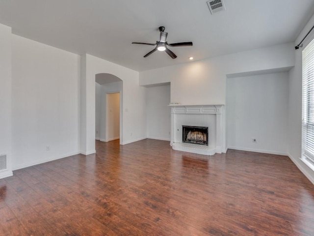 unfurnished living room with a fireplace, dark wood-type flooring, ceiling fan, and a healthy amount of sunlight