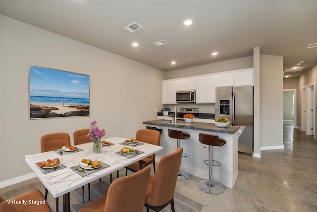 kitchen with appliances with stainless steel finishes, white cabinetry, a kitchen bar, and concrete flooring