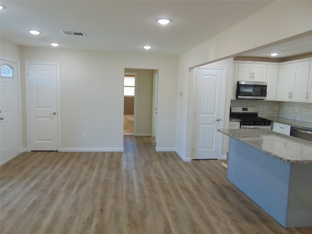 kitchen featuring white cabinetry, stainless steel appliances, light stone counters, decorative backsplash, and light hardwood / wood-style flooring