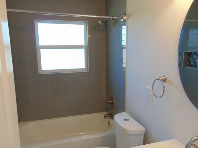 bathroom featuring toilet, plenty of natural light, and tiled shower / bath