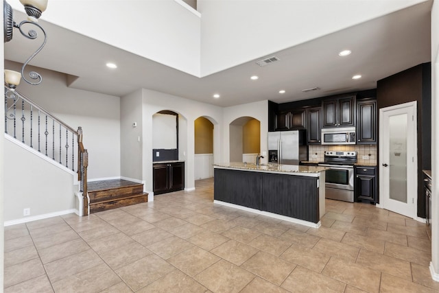 kitchen featuring sink, light tile patterned floors, an island with sink, decorative backsplash, and appliances with stainless steel finishes