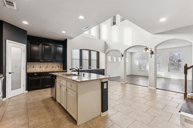 kitchen featuring dishwasher, an island with sink, light stone countertops, sink, and backsplash