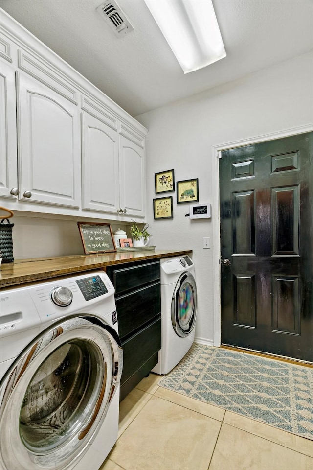 washroom with washing machine and dryer, light tile patterned floors, and cabinets