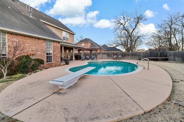 view of swimming pool with a patio, a diving board, and a trampoline