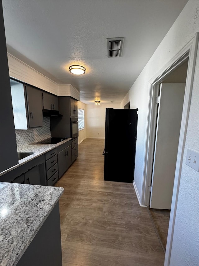 kitchen featuring a textured ceiling, light stone countertops, backsplash, dark hardwood / wood-style floors, and black appliances