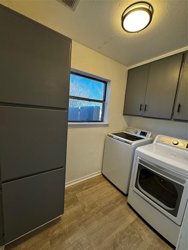 laundry room featuring washing machine and dryer, a textured ceiling, cabinets, and light hardwood / wood-style flooring