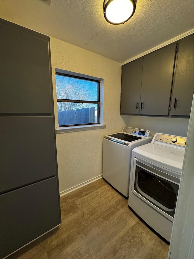 clothes washing area featuring light hardwood / wood-style floors, washing machine and clothes dryer, a textured ceiling, and cabinets