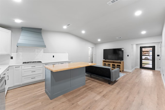 kitchen featuring custom exhaust hood, a kitchen island, stainless steel gas cooktop, wood counters, and white cabinetry