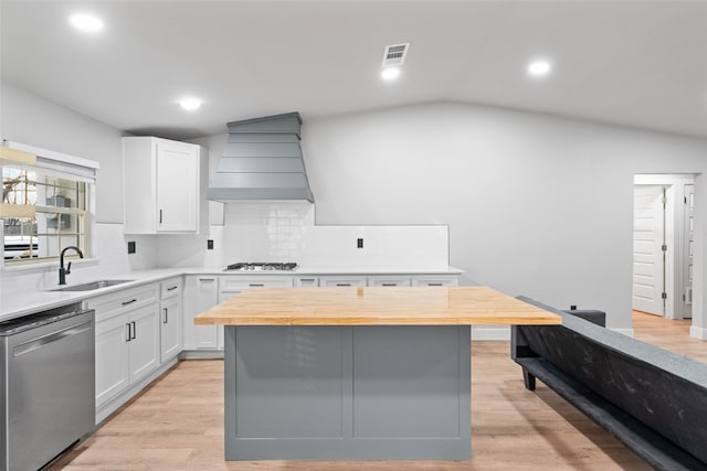 kitchen with vaulted ceiling, dishwasher, custom range hood, white cabinets, and sink