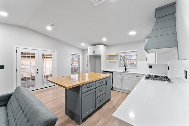 kitchen featuring white cabinets, lofted ceiling, french doors, custom exhaust hood, and butcher block countertops