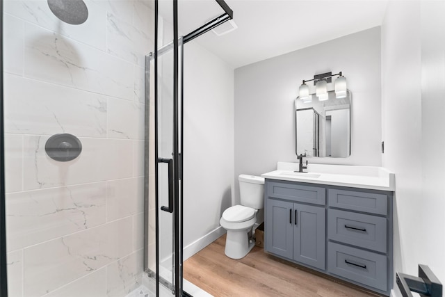 bathroom featuring toilet, hardwood / wood-style flooring, tiled shower, and vanity